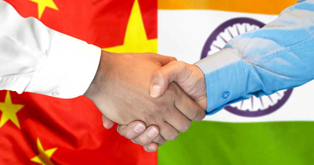 Sfondo con le 2 bandiere, cinese e indiana, con davanti Xi Jinping e Modi che si stringono la mano