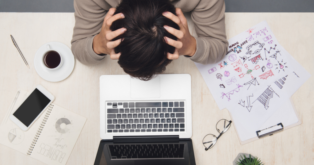 man at his desk taking his head in his hands because he has too much work